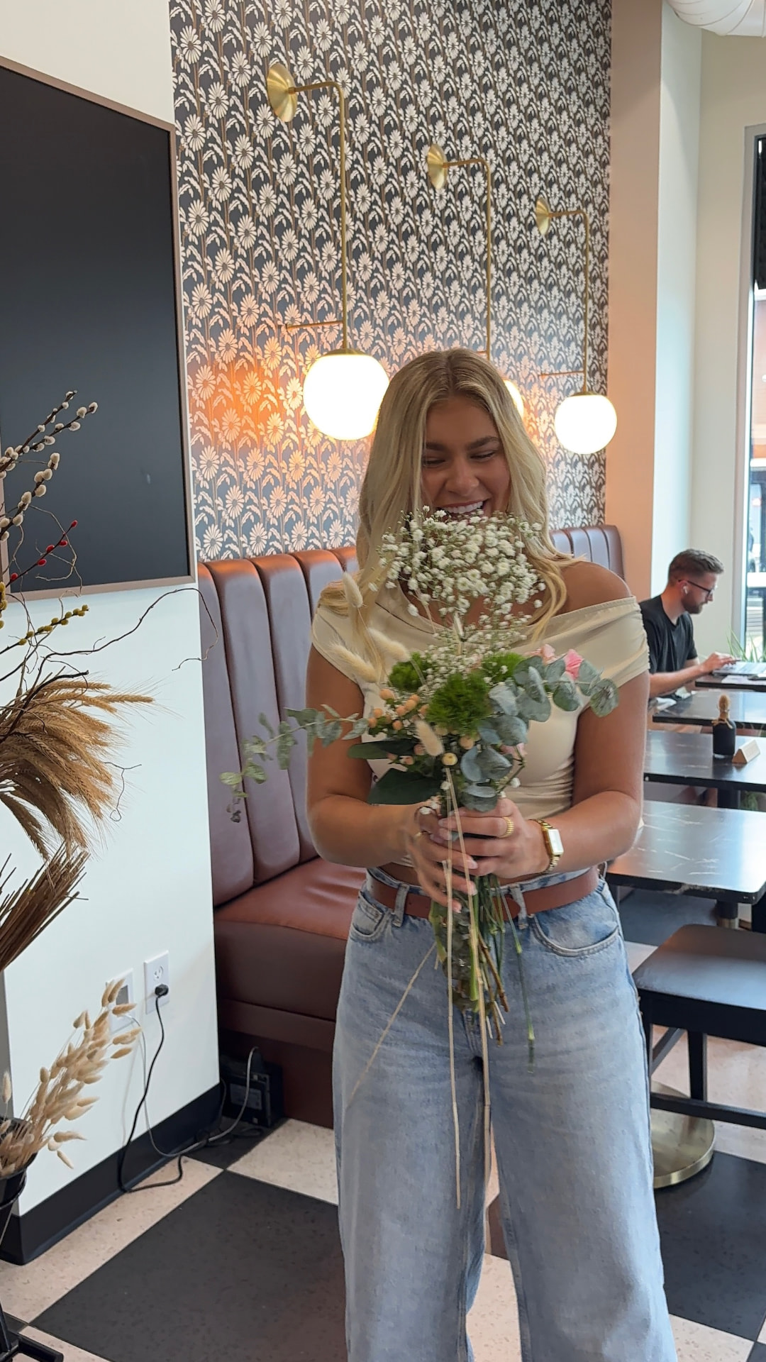 A guest laughing while holding her finished bouquet of baby's breath, eucalyptus, and bunny tails in the café