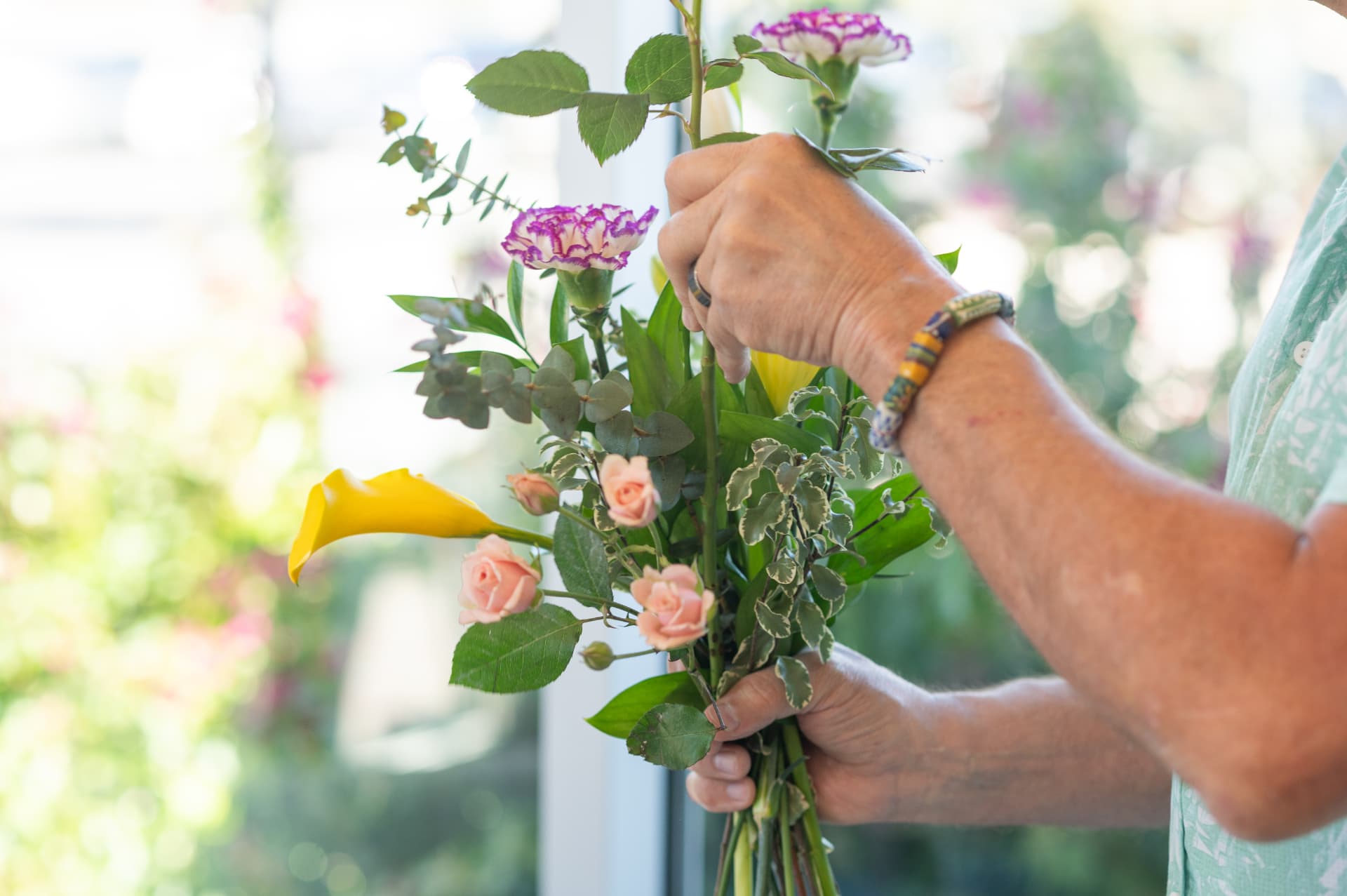 Hands gathering roses and eucalyptus into a hand-tied bouquet at the flower bar