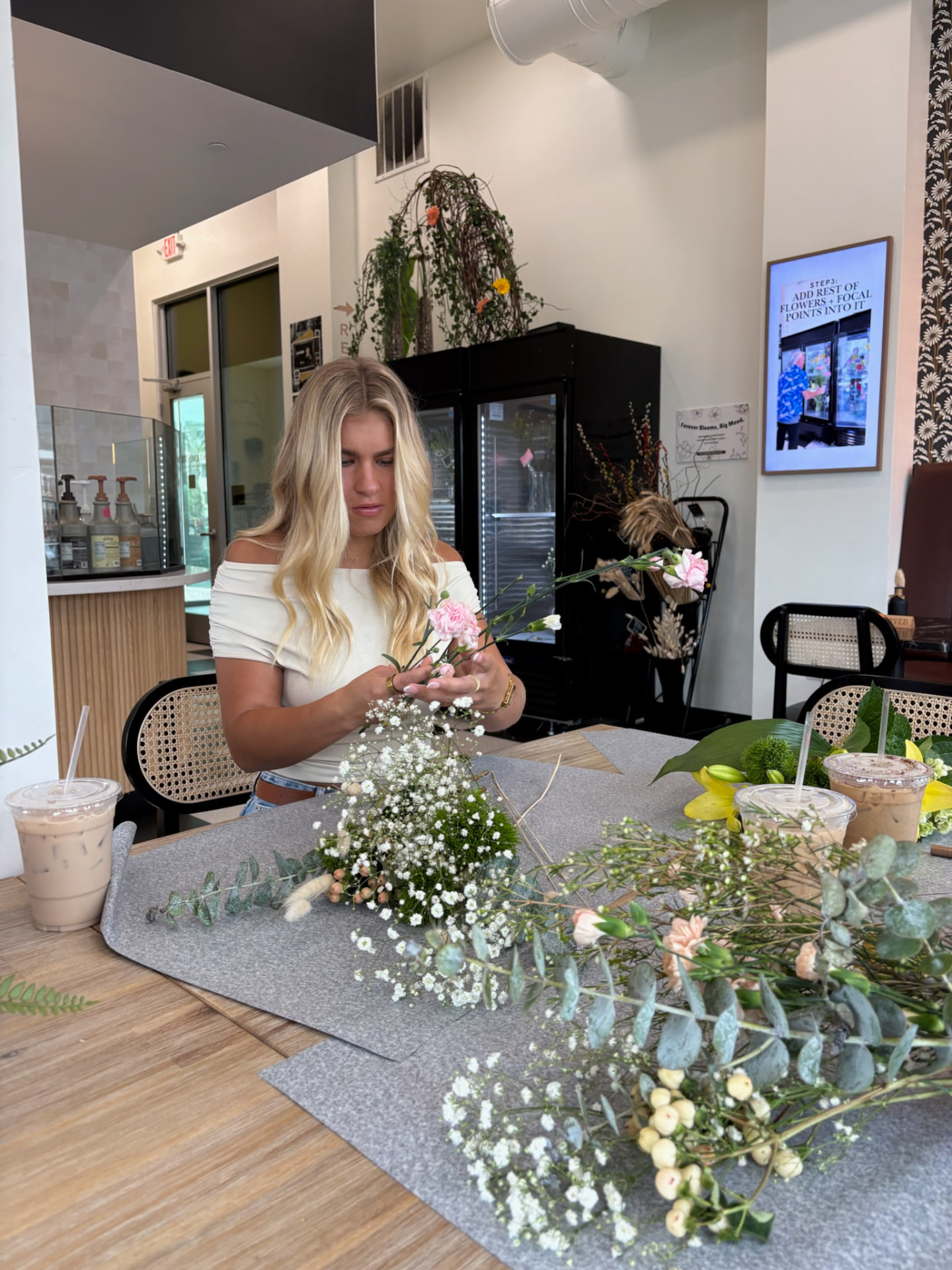 Guest arranging carnations at a table with iced coffees at Stemistry