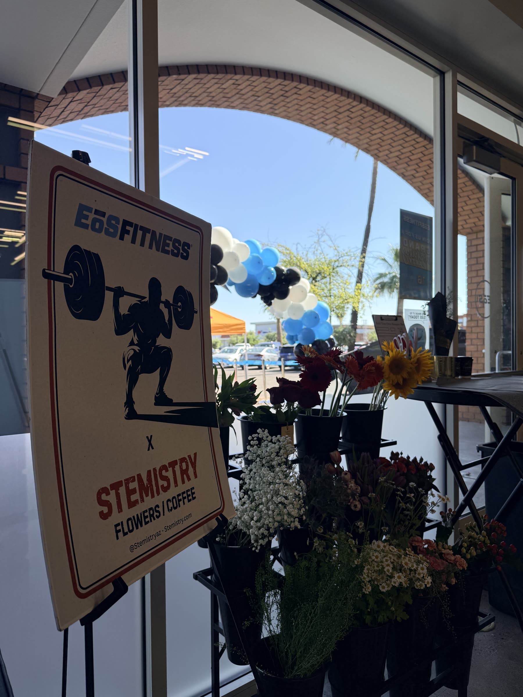 EōS Fitness x Stemistry sign at a gym grand opening with a balloon arch and flower buckets