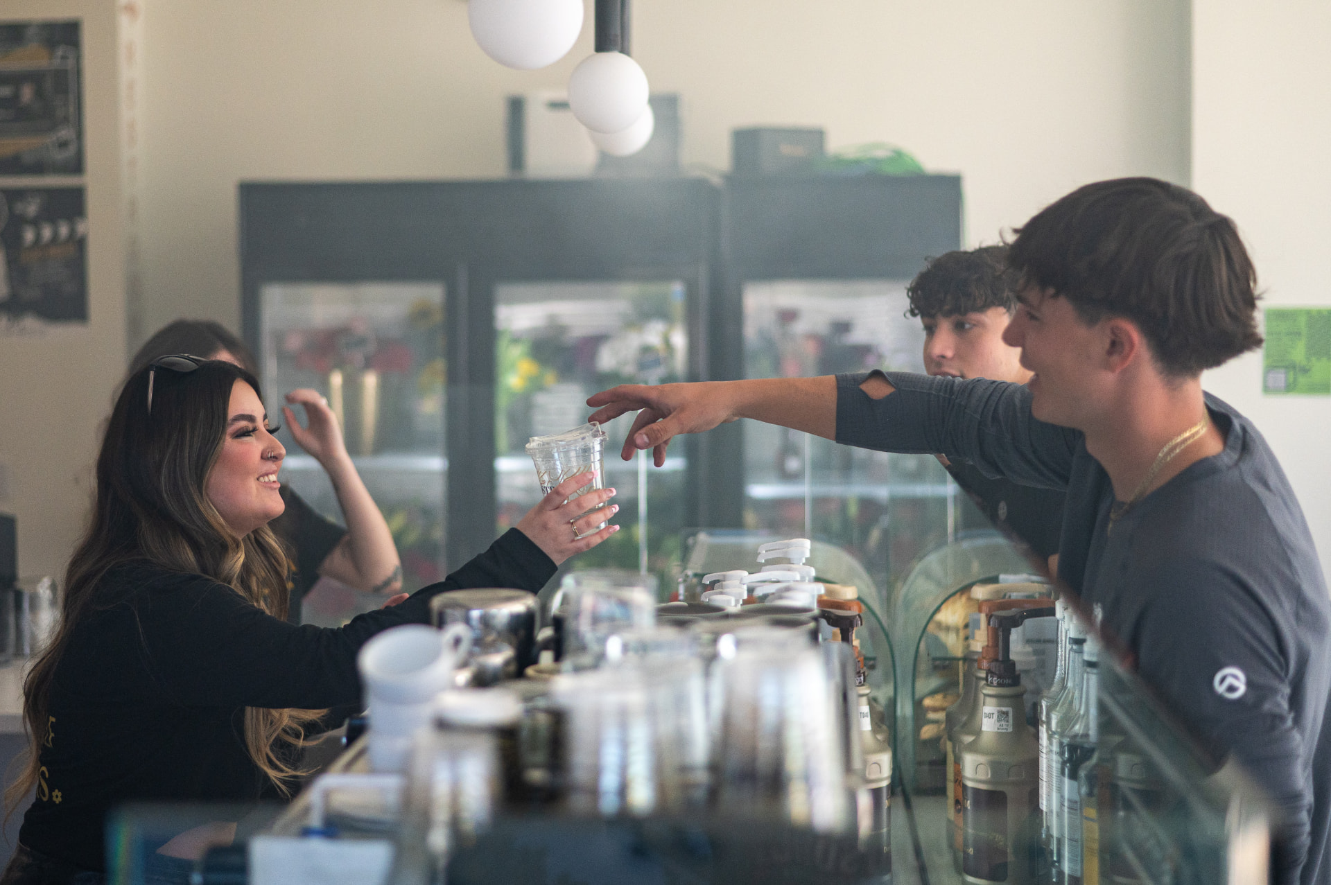 A barista handing a finished iced drink across the counter to guests at Stemistry